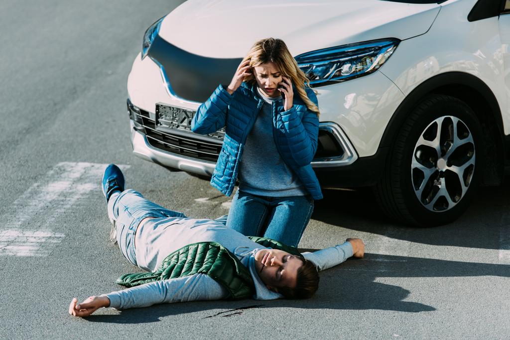 високий кут зору на налякану молоду жінку, яка дивиться на пораненого чоловіка і викликає екстрену допомогу після автомобільної аварії
 - Фото, зображення