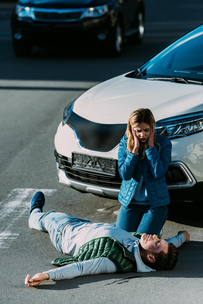 високий кут зору на налякану молоду жінку, яка дивиться на жертву, що лежить на дорозі після автомобільної аварії
 - Фото, зображення