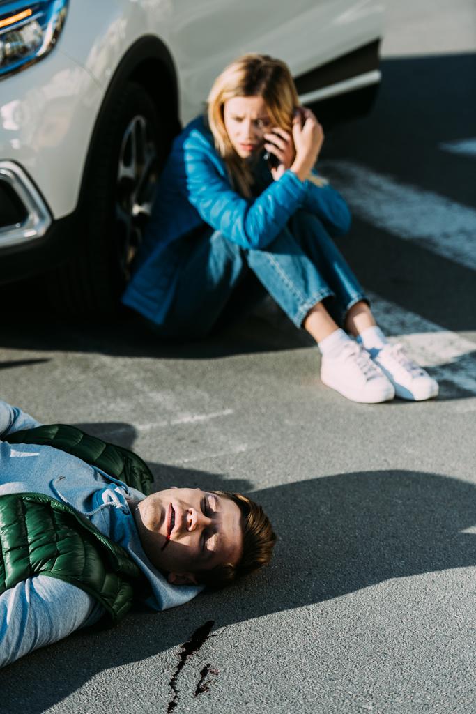 ハイアングルの怖がって若い女性の道交通衝突の後横になっている男、緊急の呼び出し  - 写真・画像