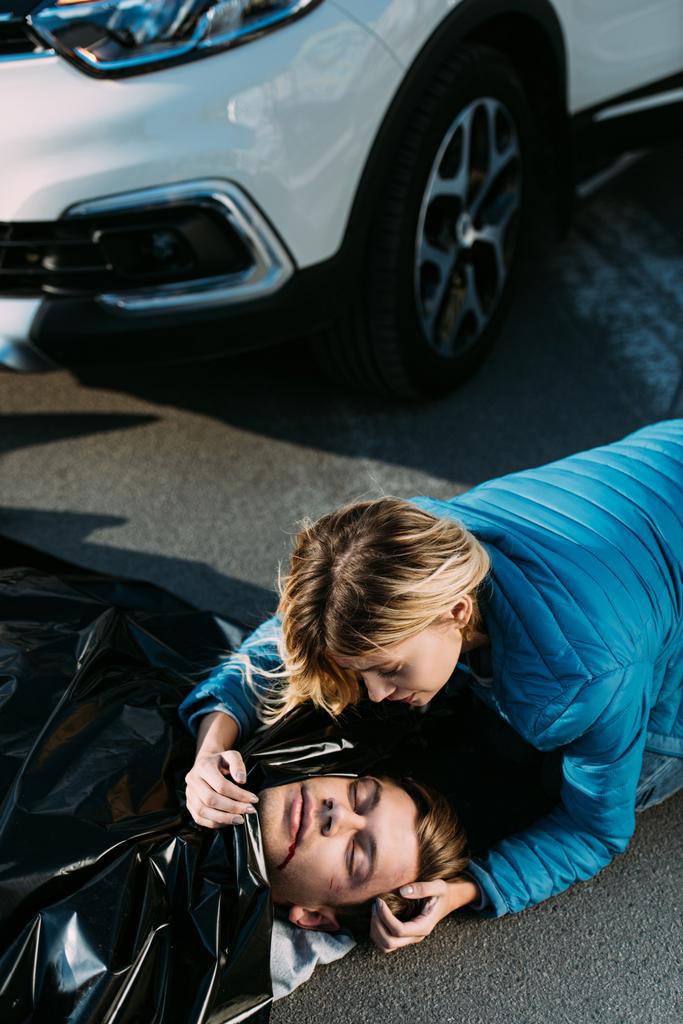 vista de ángulo alto de la mujer joven llorando sobre el hombre muerto en la carretera después de la colisión de tráfico
 - Foto, Imagen
