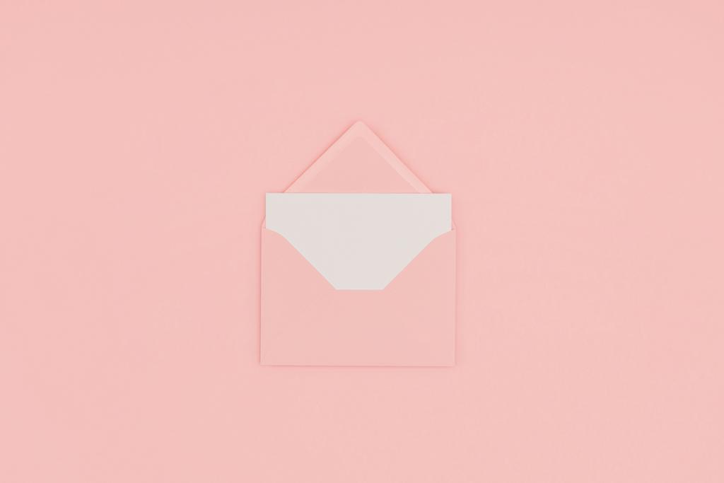 bovenaanzicht van open roze envelop met lege witte kaart geïsoleerd op roze - Foto, afbeelding