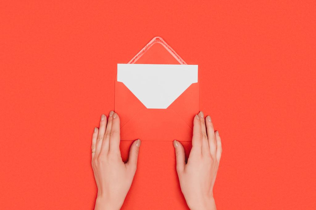 Oříznout záběr osoba otevření obálky s kartou izolované na červené - Fotografie, Obrázek