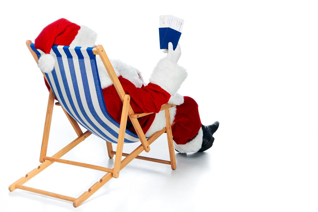 Noel Baba iki pasaport tutan görünümünü arka ve üzerinde beyaz izole beach sandalyede otururken Noel gezi için bilet hava  - Fotoğraf, Görsel
