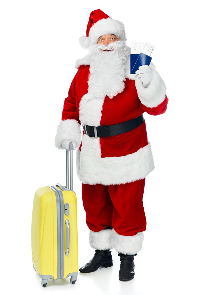 Święty Mikołaj z torba podróżna trzymając dwa paszporty i biletów lotniczych na Boże Narodzenie podróży na białym tle - Zdjęcie, obraz