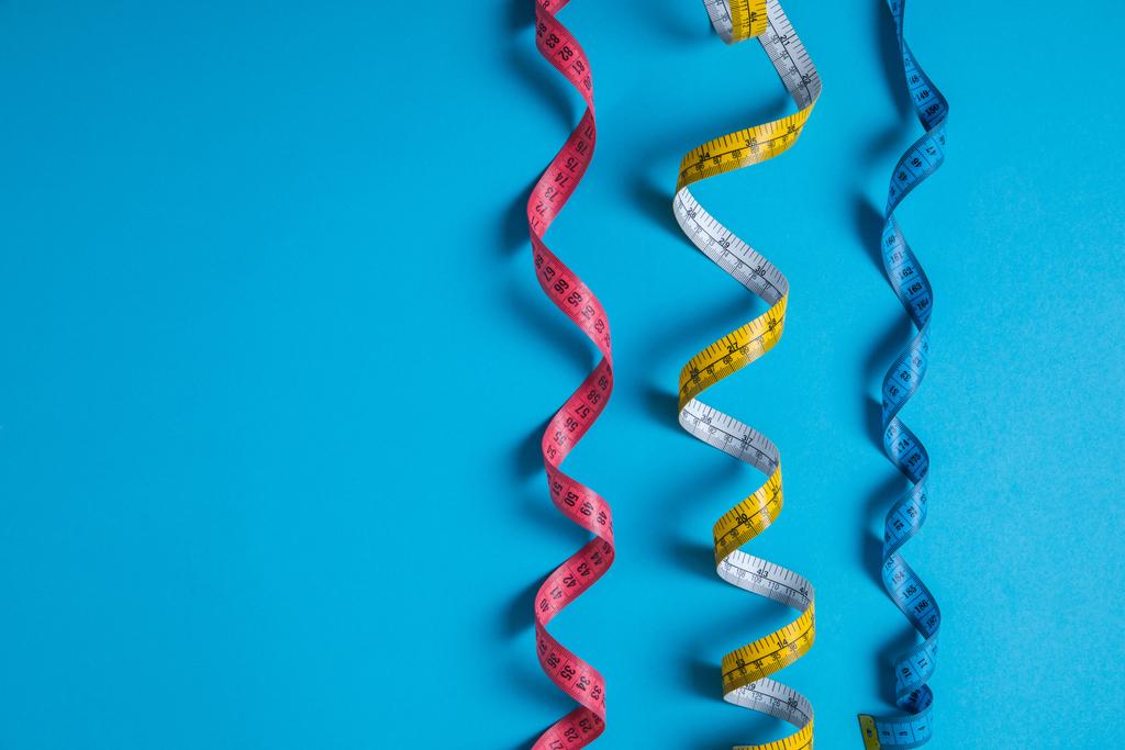 tendido plano con cintas métricas coloridas dispuestas colocadas en fila aisladas en azul
 - Foto, Imagen