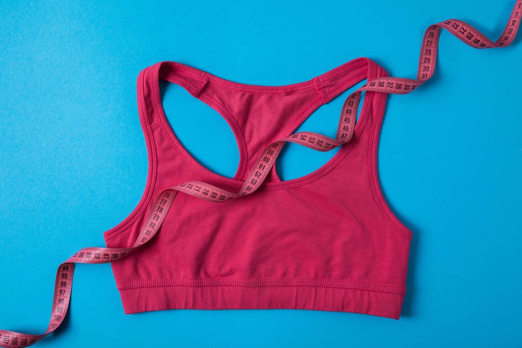 erhöhter Blick auf rosa Sport-BH und Maßband isoliert auf blauem, minimalistischem Konzept  - Foto, Bild