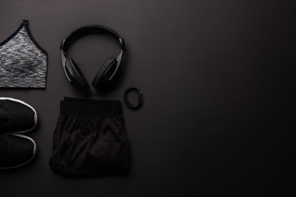 Draufsicht auf arrangierte Sportbekleidung, Kopfhörer und Fitness-Tracker isoliert auf schwarz - Foto, Bild