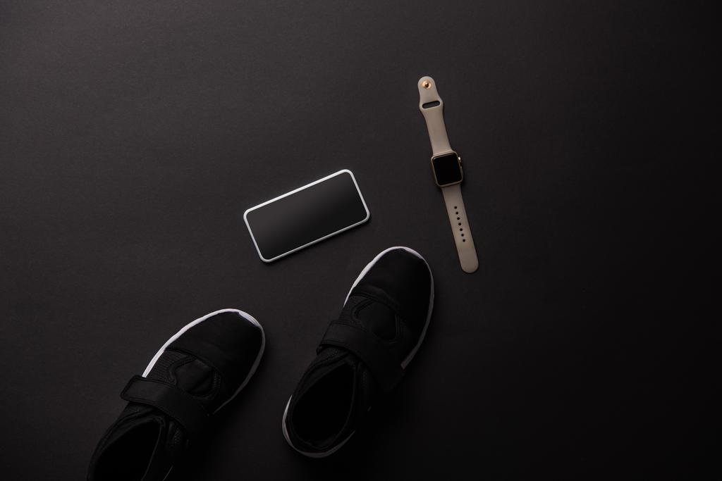 view from above of smartphone, smartwatch and sneakers isolated on black - Photo, Image