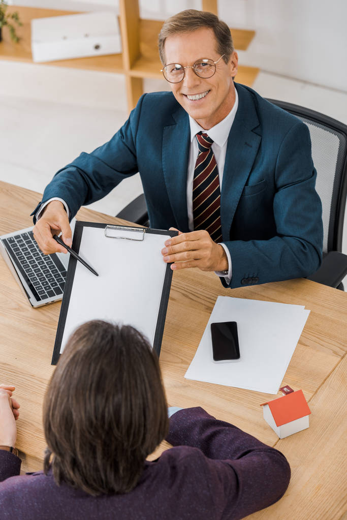 взрослый улыбающийся страховой агент в очках показывает контракт с молодым человеком в офисе
 - Фото, изображение