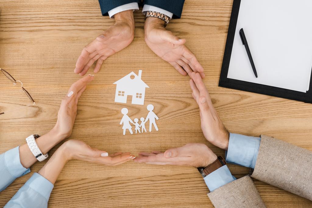 Mensen die cirkel met handen op houten tafel met papier huis en familie binnen, levensverzekeringen - Foto, afbeelding