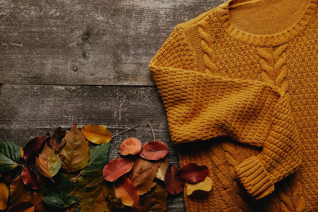 επίπεδη lay με πεσμένα φύλλα και πορτοκαλί πουλόβερ σε ξύλινη επιτραπέζια - Φωτογραφία, εικόνα