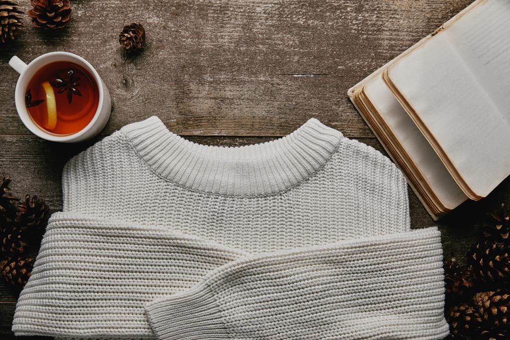 flat lay com suéter branco, cones de pinho, caderno em branco e xícara de chá na superfície de madeira
 - Foto, Imagem