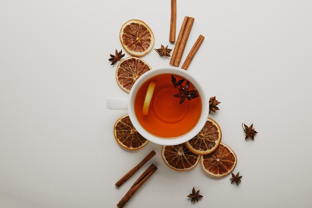 vlakke leggen met gearrangeerde kaneelstokjes, anijs sterren, gedroogde oranje stukken en kopje hete thee op witte achtergrond - Foto, afbeelding