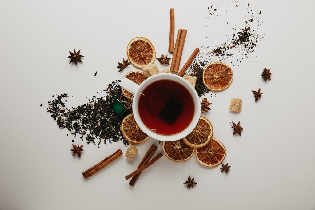flat lay with arranged cinnamon sticks, anise stars, dried orange pieces and cup of hot tea on white background - Photo, Image