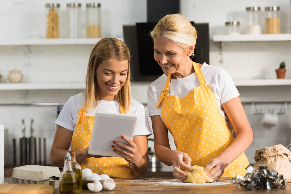 happy adult mother and daughter using digital tablet while cooking together   - Photo, Image
