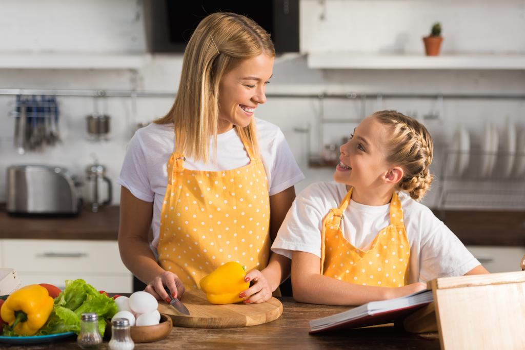 piękny szczęśliwy matka i córka uśmiechający się wzajemnie i wspólne gotowanie - Zdjęcie, obraz
