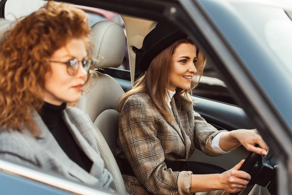fröhliche Frau mit schwarzem Hut Auto fährt, während ihre Ingwerfreundin in der Nähe sitzt  - Foto, Bild