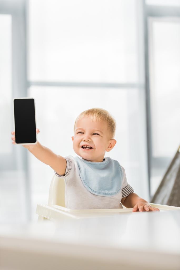şirin yürümeye başlayan çocuk holding smartphone el gülümseyen ve bebek koltuğunda oturmak - Fotoğraf, Görsel