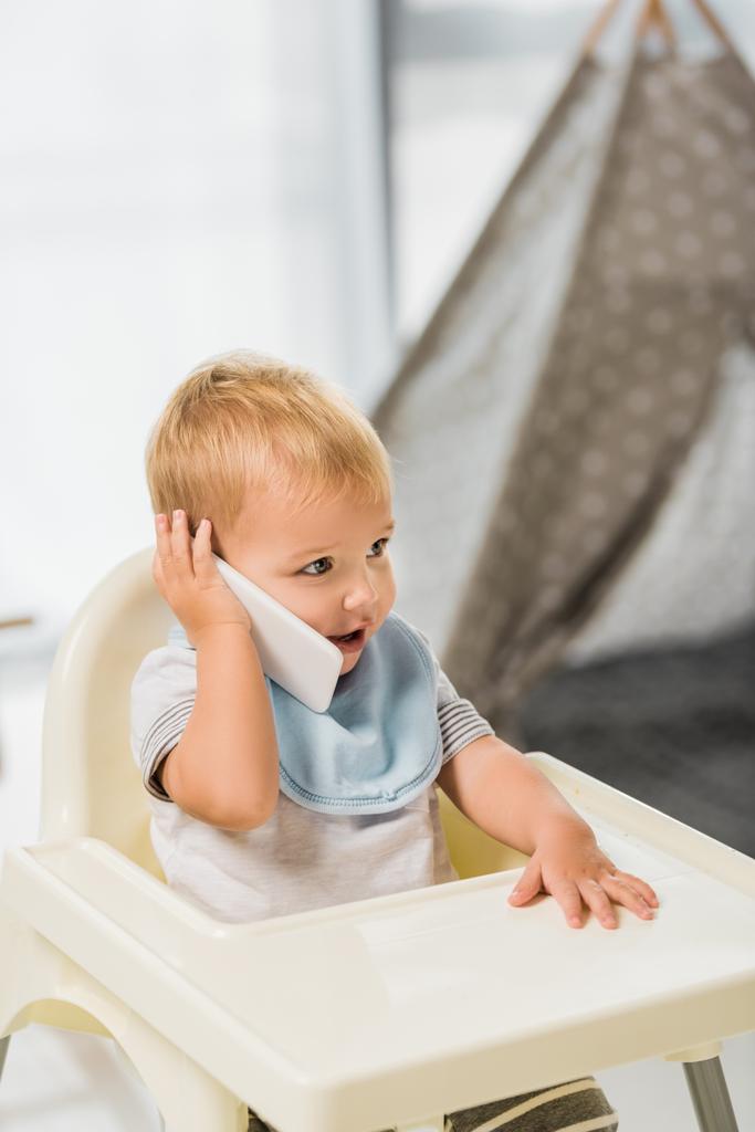 bonito criança falando no smartphone e sentado em cadeira de bebê
 - Foto, Imagem