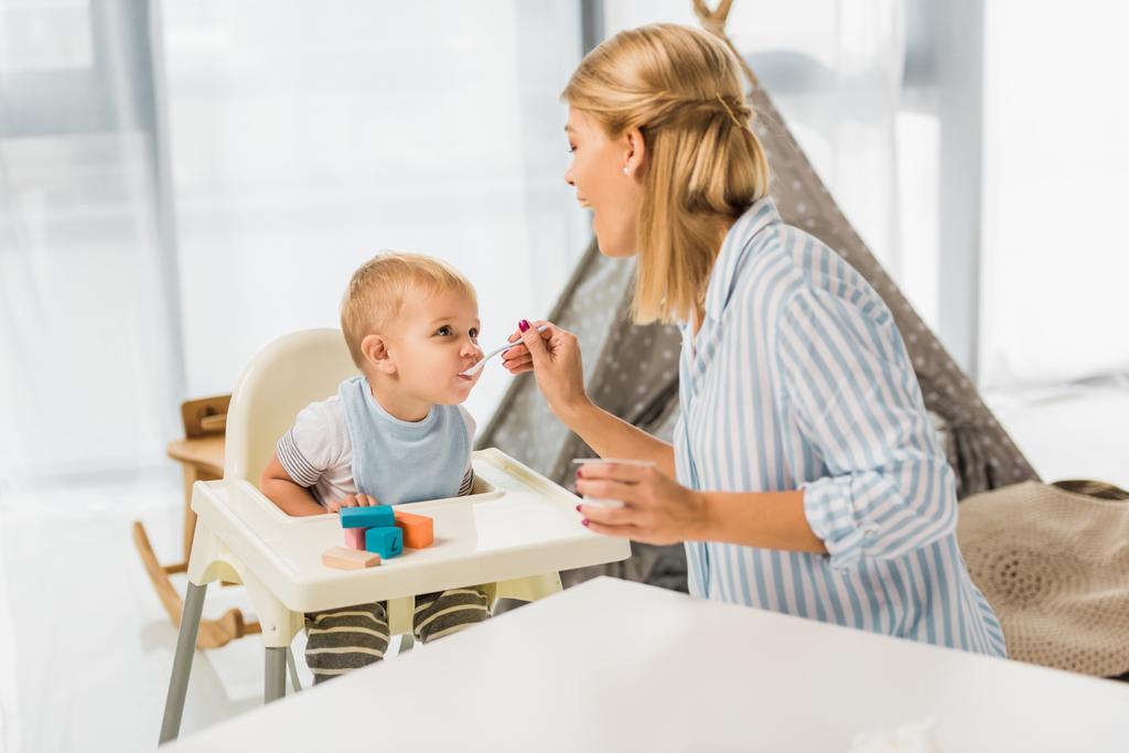 mãe alimentando filho em cadeira alta com comida de bebê
  - Foto, Imagem