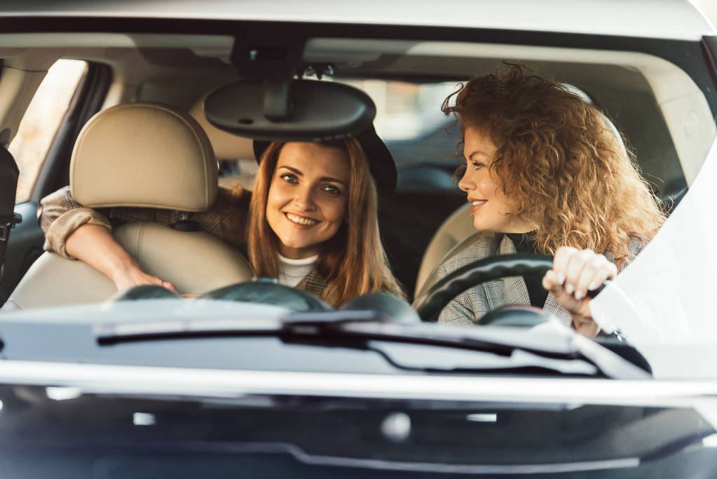 uśmiechnięta kobieta Ruda jazdy samochodem podczas jej koleżanki, siedząc na tylnym siedzeniu  - Zdjęcie, obraz