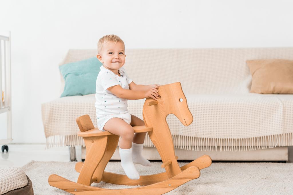 очаровательный улыбающийся малыш сидит на игрушечной деревянной лошади
 - Фото, изображение
