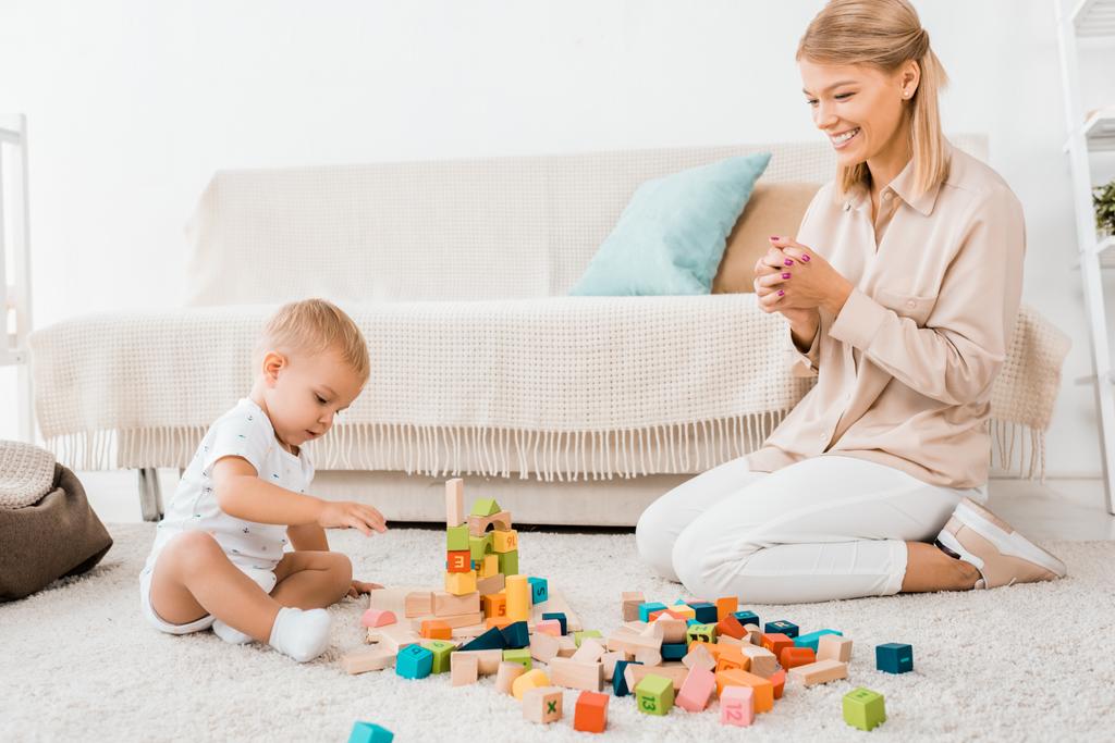 adorable toddler playing with colorful cubes and mother in nursery room - Photo, Image