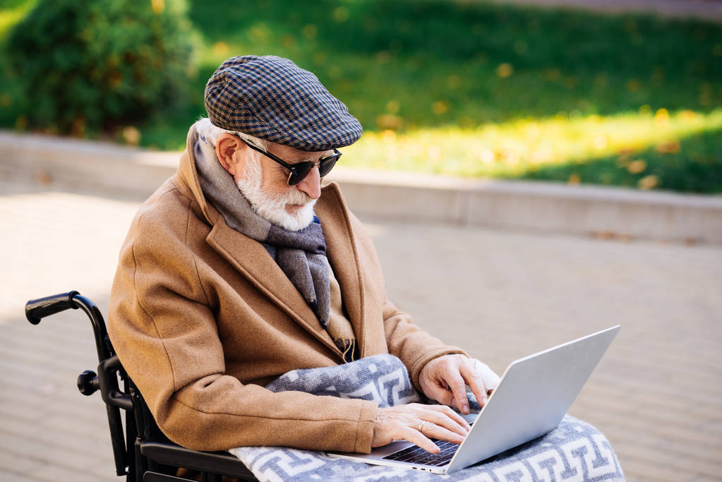 idoso deficiente em cadeira de rodas com xadrez usando laptop na rua
 - Foto, Imagem