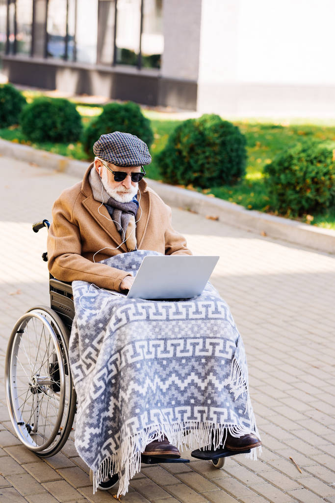 homem deficiente sénior concentrado em cadeira de rodas usando laptop na rua
 - Foto, Imagem