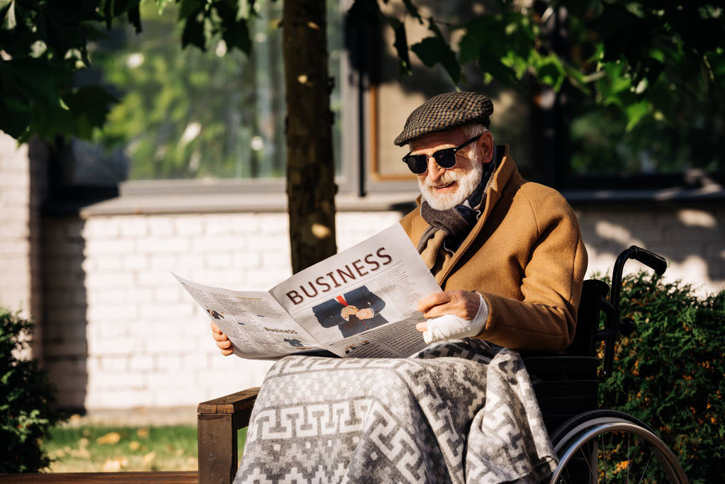 Senior uitgeschakeld man in rolstoel lezen van zakelijke krant op straat - Foto, afbeelding