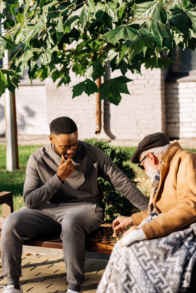 anciano y joven afroamericano cuidador jugando ajedrez juntos en la calle
 - Foto, imagen