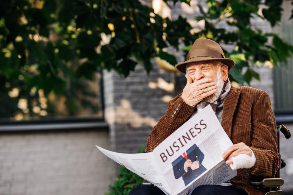 χασμουρητό ανώτερος ανίκανος άνθρωπος σε τροχοκάθισμα ανάγνωση επιχειρηματική εφημερίδα στην οδό - Φωτογραφία, εικόνα