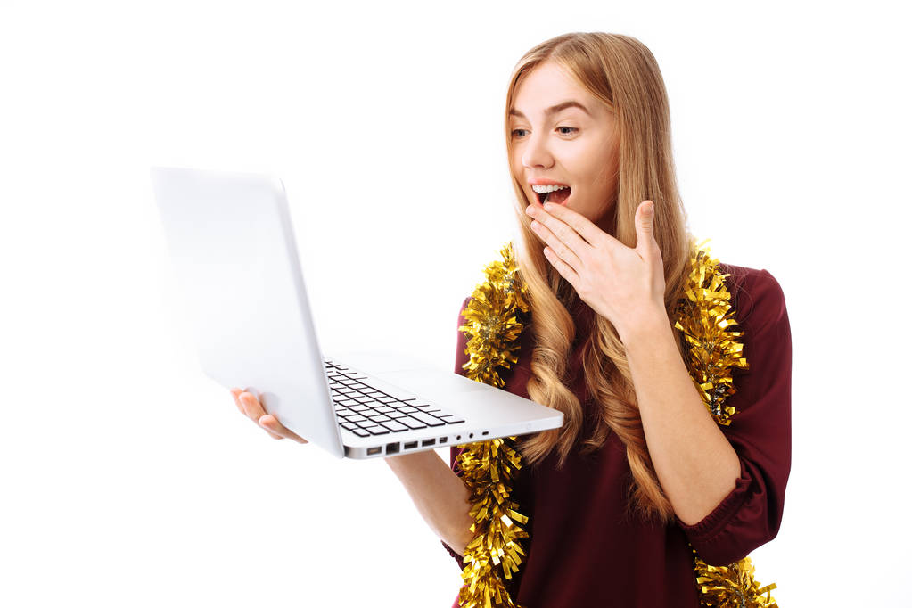 Šokovaný, dívka v červených šatech používá přenosný počítač a s překvapením, na bílém pozadí se dívá na obrazovku notebooku. Vánoční - Fotografie, Obrázek