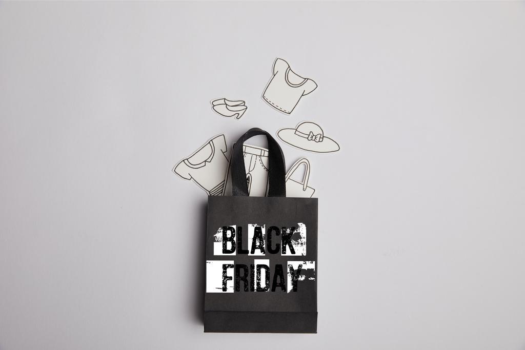 κάτοψη του μαύρη τσάντα για ψώνια με μαύρη Παρασκευή επιγραφή και χαρτί ρούχα σε γκρι φόντο - Φωτογραφία, εικόνα