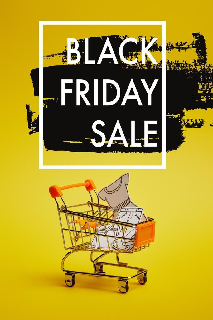 close up vista de pouco carrinho de compras com roupas de papel no fundo amarelo, inscrição venda sexta-feira preta
 - Foto, Imagem