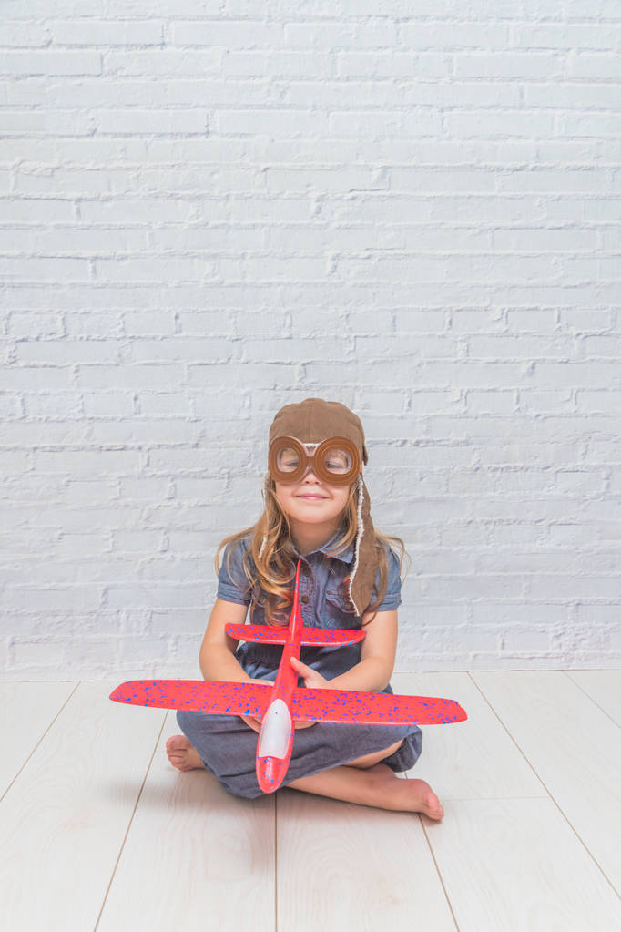 una niña, niño en el casco del piloto con el avión y luces en el vidrio delante de una pared de ladrillo blanco
 - Foto, imagen