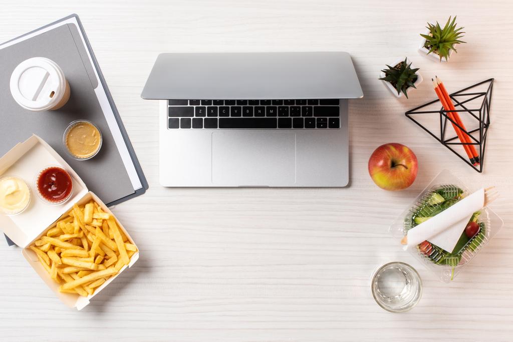 vista superior de la computadora portátil, comida saludable y comida chatarra en el lugar de trabajo
 - Foto, Imagen