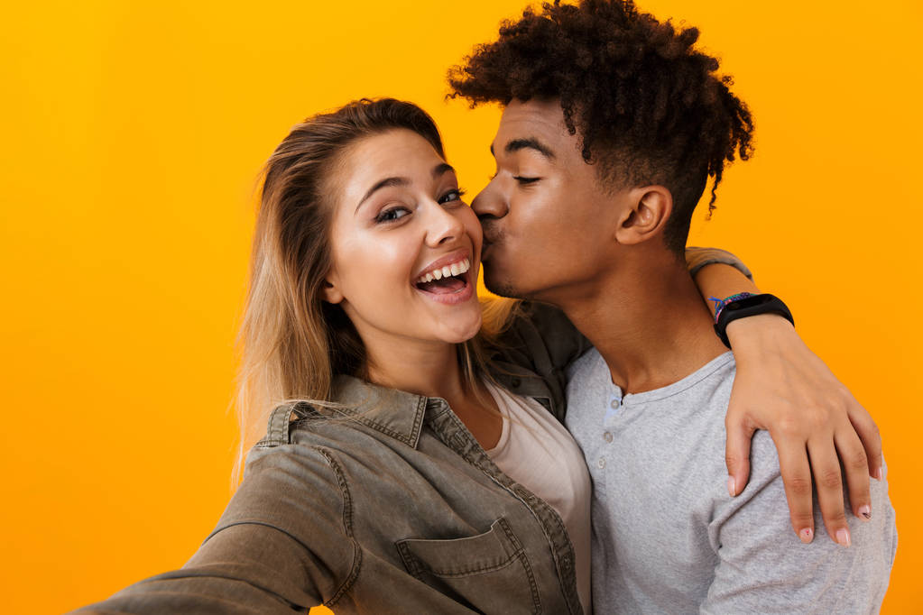 Boldog aranyos fiatal szerető pár jelentő képe elszigetelt sárga háttér átölelve veszi át a selfie kamera csók. - Fotó, kép