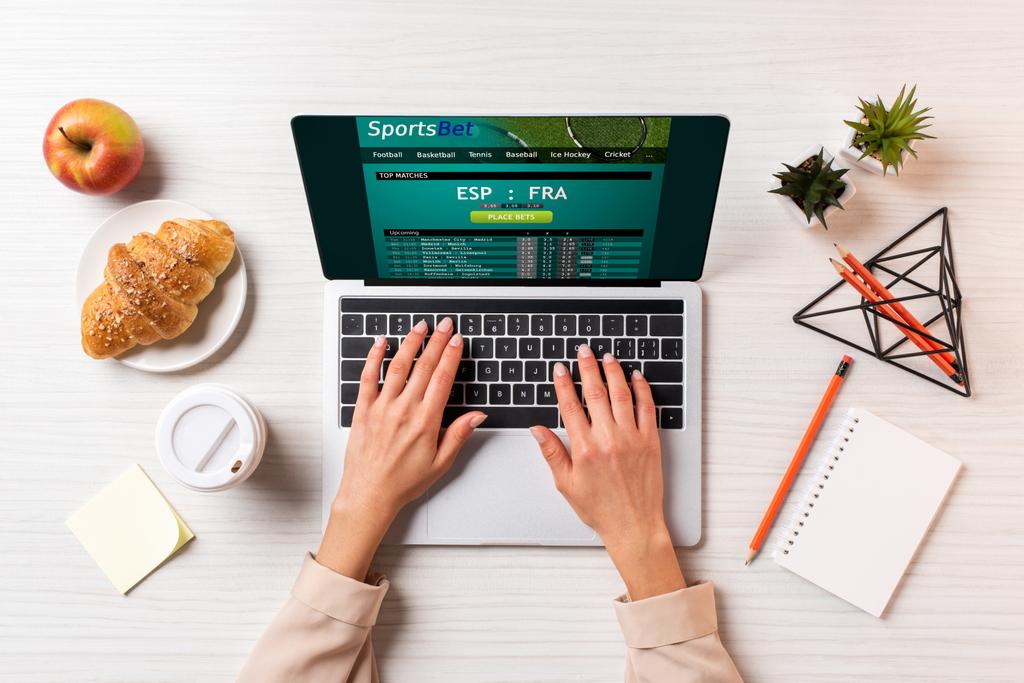 colpo ritagliato di donna d'affari utilizzando il computer portatile con scommesse sportive sito web a tavola con caffè, mela e croissant
     - Foto, immagini