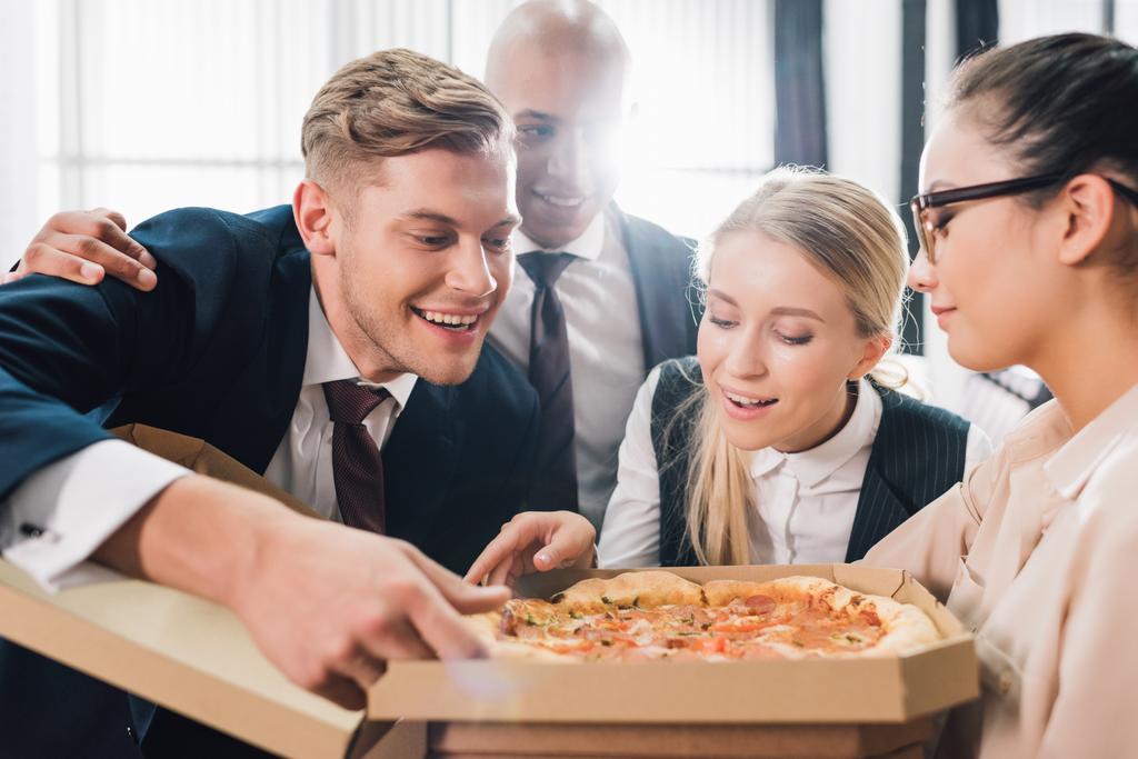 усміхнені молоді колеги дивляться на смачну піцу в офісі
   - Фото, зображення