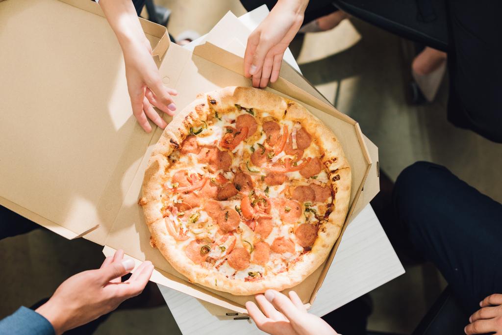 частичный вид сверху на коллег, поедающих пиццу в офисе
  - Фото, изображение