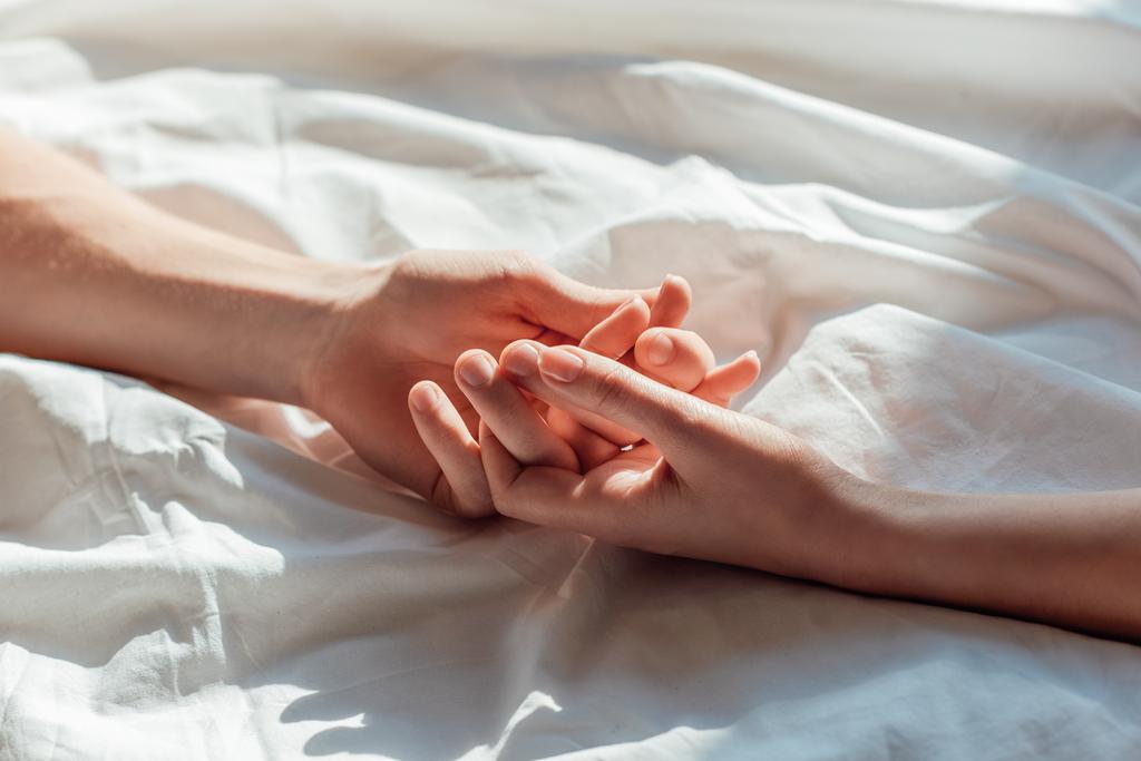 Teilansicht eines Paares in lebender Hand, während es zusammen im Bett liegt - Foto, Bild