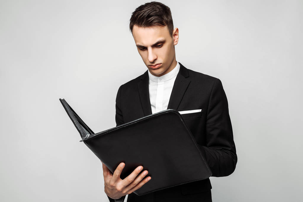 Úspěšný muž v černém obleku se složkou v ruce, práci s dokumenty na šedém pozadí. - Fotografie, Obrázek
