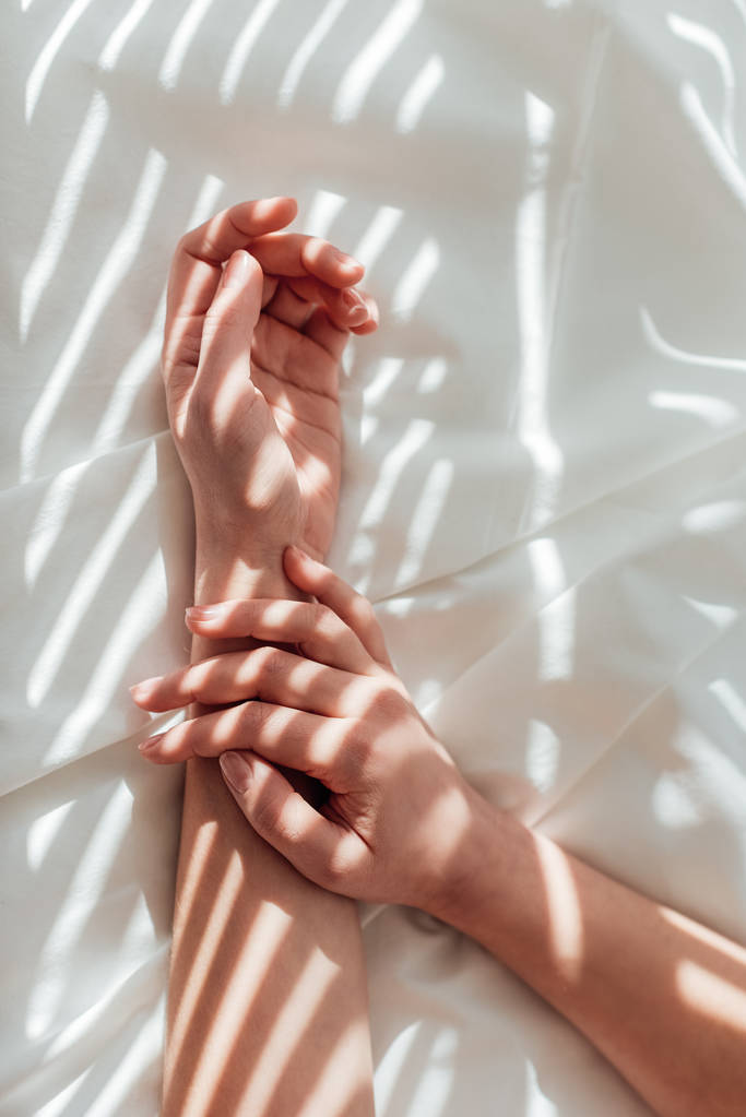 обрезанный снимок женских рук на белом простыне
 - Фото, изображение