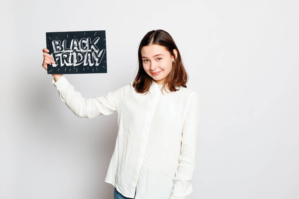 Nakupování, maloobchodní, černý pátek prodej, nakupování a lidé koncept - mladá usměvavá brunetka drží znak černý pátek. Černý pátek prodej. - Fotografie, Obrázek