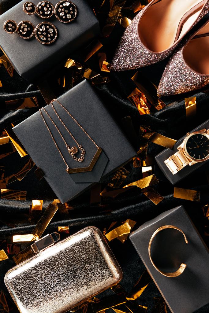 vlakke leggen met vrouwelijke schoenen, handtas en juwelen op zwarte achtergrond met gouden confetti  - Foto, afbeelding