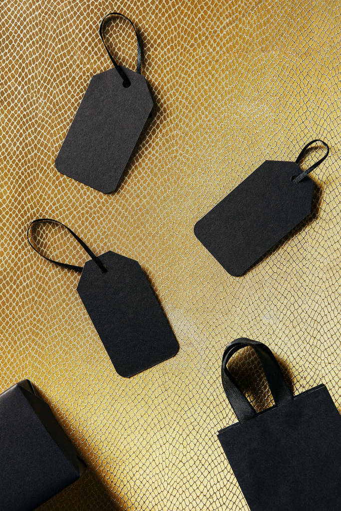pohled shora černé prázdné cenovek, krabice a tašky na zlaté pozadí, černý pátek koncept - Fotografie, Obrázek