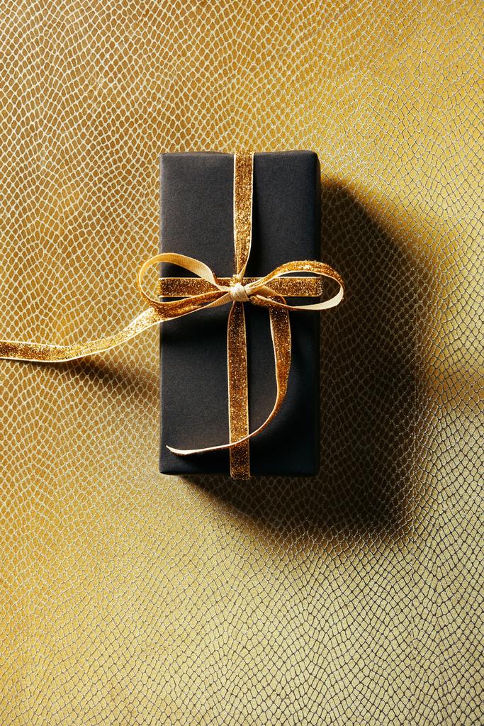 top view of wrapped gift box with golden ribbon on golden background - Photo, Image