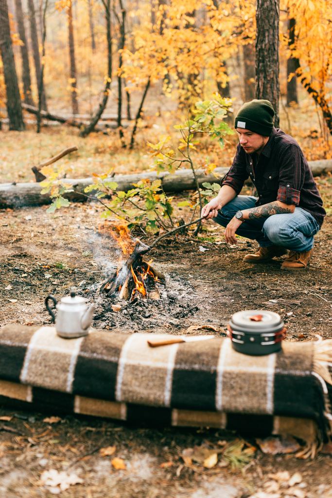 дорослий чоловік готує їжу вогнем на відкритому повітрі в осінньому лісі
 - Фото, зображення