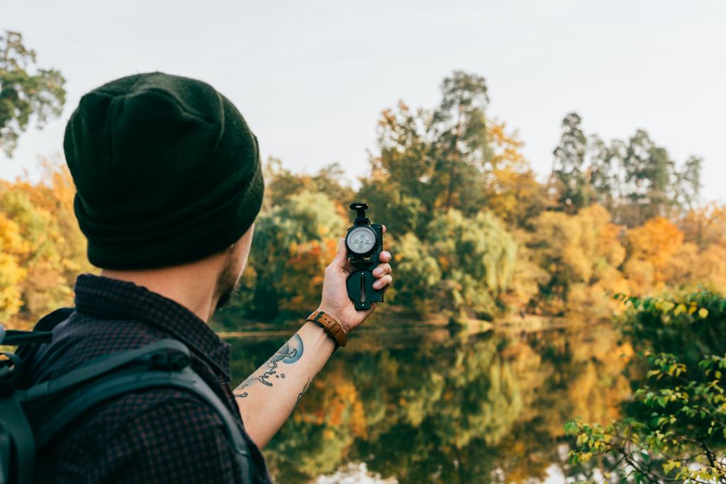 male traveller with backpack holding compass on autumnal background - Photo, Image